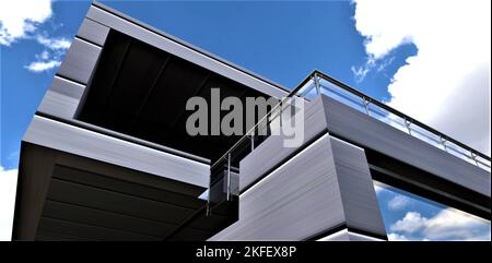 Blick von unten auf die Aluminiumfassade eines zweistöckigen Landhauses in einem futuristischen Stil mit großen Panoramafenstern und einem Balkon gegen ein wolkiges sk Stockfoto