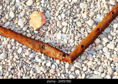 Alte verwitterte Metallrohre mit verrosteten Strukturen, die auf einem Kieselstrand ruhen Stockfoto