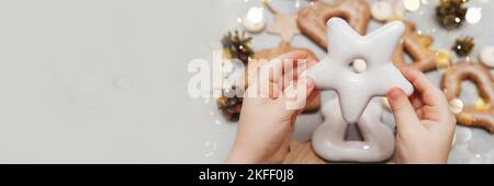 Die Hände der Kinder halten einen Lebkuchen in Sternform. Das Konzept von Weihnachtsbonbons, Spielzeug, Girlanden und Bokeh. Einrichtung für Neujahrsferien. Stockfoto