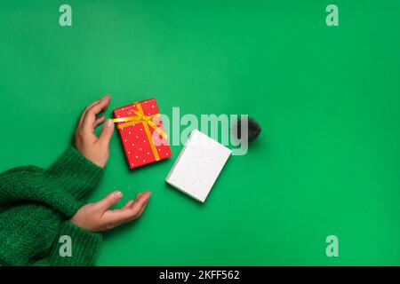 Frauenhände mit schwebender Geschenkschachtel und dekorativem weihnachtsbaum, Draufsicht auf grünem Hintergrund. Weihnachtsgeschenke Vorbereitungskonzept Stockfoto