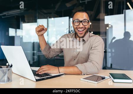 Porträt eines erfolgreichen hispanischen Führers, lächelnder Mann in der Brille und Blick auf die Kamera, der die Hand hochhält und die Geste des Erfolgs, des guten Arbeitsergebnisses, des Sieges und des Triumphs zeigt. Stockfoto