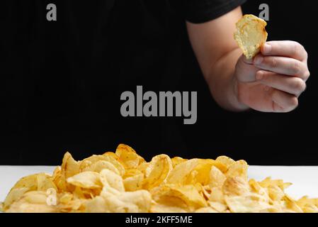 Der Mann isst Junk Food, Chips auf dunklem Hintergrund. Schädliche Lebensmittel. Frittierte Lebensmittel sind schlecht für Ihre Gesundheit. Gesunde Lebensweise, richtige Ernährung, Verbot Stockfoto