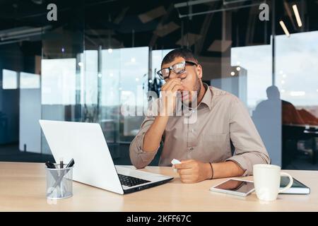 Übermüder Büroangestellter in Brille, der mit einem Laptop im Büro arbeitet, Geschäftsmann Manager, der spät arbeitet. Stockfoto