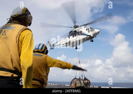 220915-N-XN177-2055 PHILIPPINISCHES MEER (SEPT 15, 2022) – ein AS-332 Super Puma-Hubschrauber liefert während einer Auffüllung auf See mit dem Militärischen Sealift Command Trockenfracht- und Munitionsschiff USNS Carl Brashear (T-AKE 7) am 15. September 2022 eine Ladung an den amphibischen Angriffsträger USS Tripoli (LHA 7). Tripolis ist im Einsatzgebiet der US-Flotte von 7. tätig, um die Interoperabilität mit Verbündeten und Partnern zu verbessern und als einsatzbereite Einsatztruppe für den Frieden und die Stabilität in der Region Indo-Pazifik zu dienen. Stockfoto