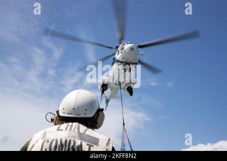 220915-N-XN177-2303 PHILIPPINISCHES MEER (SEPT 15, 2022) – ein AS-332 Super Puma-Hubschrauber liefert während einer Auffüllung auf See mit dem Militärischen Sealift Command Trockenfracht- und Munitionsschiff USNS Carl Brashear (T-AKE 7) am 15. September 2022 eine Ladung an den amphibischen Angriffsträger USS Tripoli (LHA 7). Tripolis ist im Einsatzgebiet der US-Flotte von 7. tätig, um die Interoperabilität mit Verbündeten und Partnern zu verbessern und als einsatzbereite Einsatztruppe für den Frieden und die Stabilität in der Region Indo-Pazifik zu dienen. Stockfoto