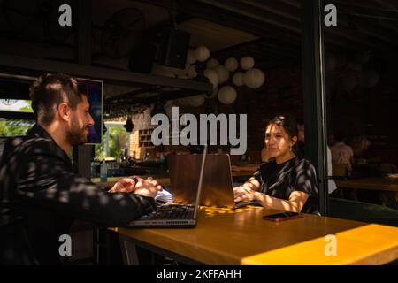 Ein glücklicher Geschäftsmann entspannt sich, während seine Kollegin auf ihrem Schoß in einer Kaffeebar arbeitet Stockfoto