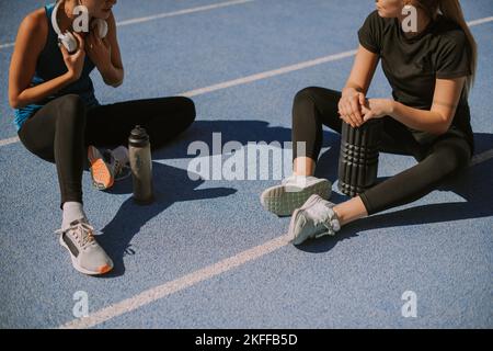 Zwei schöne Mädchen ruhen sich nach dem Laufen im Stadion aus. Sie führen ein Gespräch Stockfoto