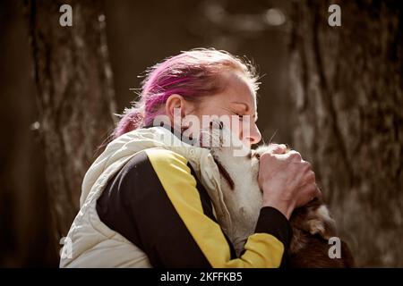 Frau mit rosa Haaren umarmt sibirischen Husky Hund, wahre Liebe zum Besitzer und Haustier, lustige Emotionen der braunen Husky Hund und Besitzer. Mädchen umarmt geliebten Husky Hund Stockfoto