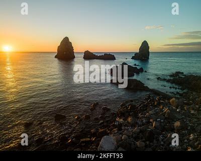 Luftdrohnenansicht von Aci Trezza bei Sonnenaufgang, Lachea Island und den Ciclope Stacks bei Sonnenuntergang. Sizilien, Italien Stockfoto