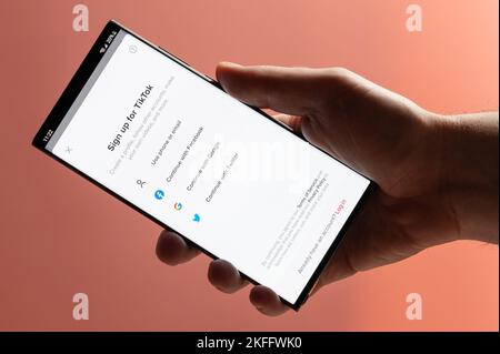 New york, USA - 10. November 2022: Melden Sie sich für TikTok auf dem Smartphone an, das die Nahaufnahme auf einem rosa Hintergrund in der Hand hält Stockfoto