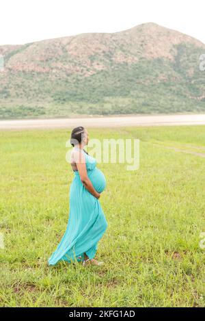 Eine schwangere Mutter, die ihren wachsenden, schwangeren Bauch hält und die Vorfreude auf die Geburt ihres Babys genießt Stockfoto