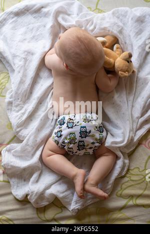 Ein glückliches, zufriedenes Baby, das auf dem Bauch liegt und in der Bauchlage sitzt, um ihren Rücken zu stärken. Sie trägt eine moderne, wiederverwendbare Stoffwindel Stockfoto