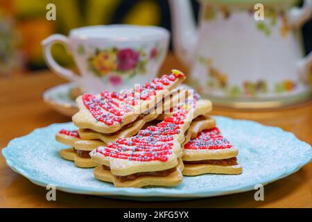 Eine Nahaufnahme von rosa verzierten Weihnachtsbaumblätzchen, die auf dem weißen Teller serviert werden Stockfoto