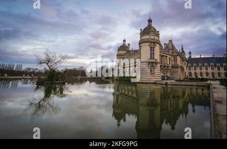 Domaine de Chantilly, Schloss Chantilly bei Sonnenuntergang, Spiegelung des Wolkenhimmels im Teich. Berühmtes Touristenziel in der Nähe von Paris. Stockfoto