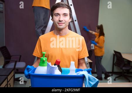 Freundliches Reinigungspervium, das lächelt und Chemikalien hält Stockfoto