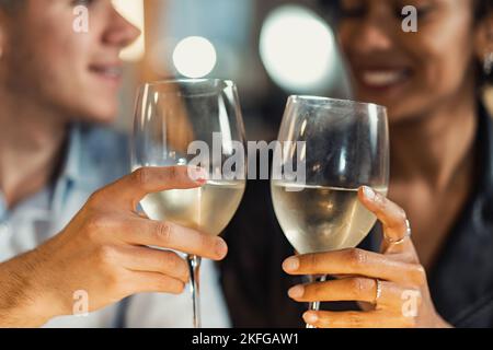 Gemischtes Paar auf Verabrat im Restaurant, lächelnd und klirrender Weißwein - multirassischer Mann und Frau, die Spaß haben, zusammen zu trinken und zu essen Stockfoto