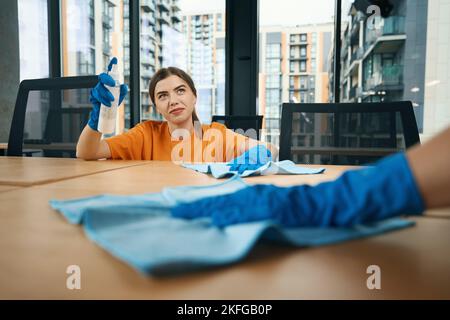 Nette Mitarbeiter der Reinigungsfirma in Gummischutzhandschuhen desinfizieren Desktops Stockfoto