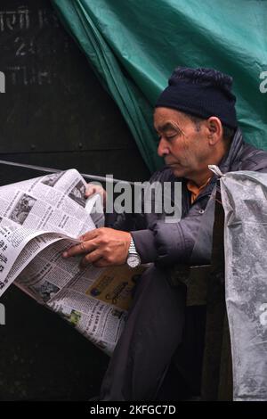 Gangtok, INDIEN, 22. Juni 2022, Mann mittleren Alters liest Zeitung am Straßenrand. Stockfoto