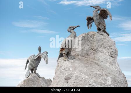 Morecambe Bay direkt am Meer. Drei Metallkunstskulpturen von Kormoranen saßen auf den grauen Steinfelsen. Schöner blauer Himmel Hintergrund. Stockfoto