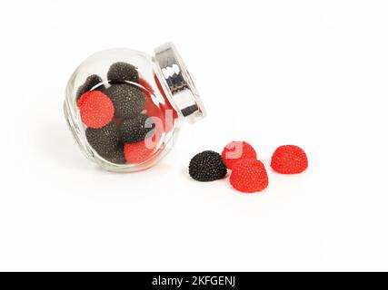 Süße schwarze und rote Fruchtsaftjellies in Form von Brombeeren und Himbeeren innen und aus einem Glas. Stockfoto