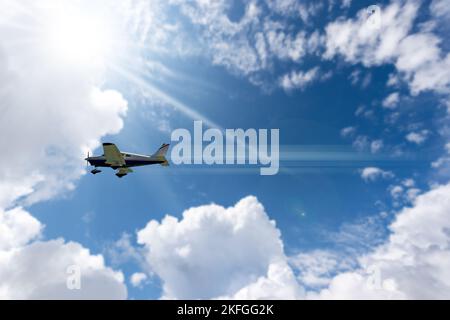 Kleines privates Propellerflugzeug in Bewegung gegen einen schönen klaren blauen Himmel mit Kumuluswolken und Sonnenstrahlen. Stockfoto