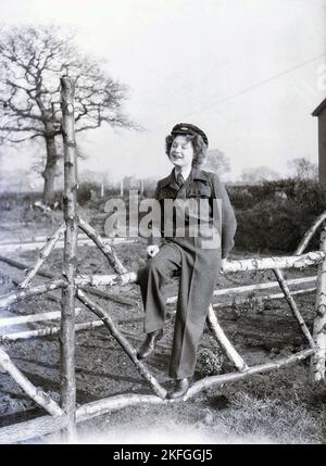 1940er Jahre, historisch, posierte für ein Foto auf einem Zaun außerhalb von Longford Camp, im RAF Tern Hill in der Nähe von Market Drayton, Shropshire, England, UK, eine junge WAAF-Frau mit Kragen und Krawatte, Tunika aus Wollstoff und Hose und Hut. Die Women's Auxillary Air Force (WAAF) wurde im Juni 1939 gegründet, wobei die Rekruten zwischen 18-43 Jahren alt waren. Stockfoto