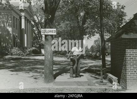 Trinkbrunnen auf dem Rasen des Bezirksgerichts, Halifax, North Carolina, 1938-04. Afroamerikanischer Junge, der an einem abgetrennten Trinkbrunnen neben einem Schild mit der Aufschrift steht. Stockfoto