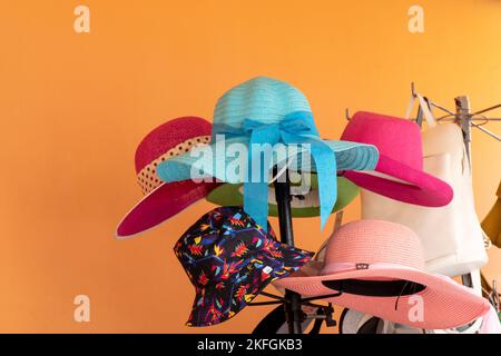 Sammlung von bunten Sommerhüten auf einem Hutständer vor leuchtend orangefarbenem Hintergrund gehängt Stockfoto