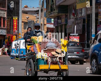 Desaguadero, Peru - Juli 28 2022 - Peruanischer Mann fährt auf der Straße auf einem Dreirad mit einer indigenen Frau und ihren Markttaschen Stockfoto