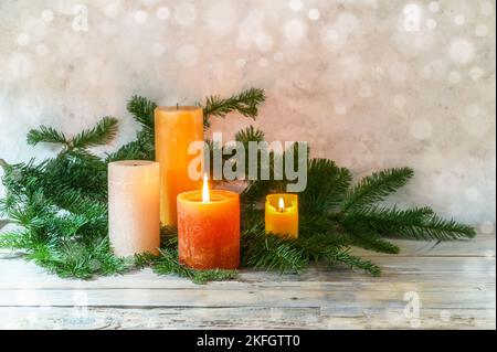 Zweiter Advent, Arrangement mit vier Kerzen in orange und gelb, zwei davon mit einer Flamme angezündet, Tannenzweige auf hellem rustikalem Holz, Bokeh-Hintergrund, Kopie Stockfoto