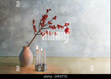 Minimalistisches zweites Advent mit vier kleinen Kerzen, zwei brennenden und einem Beerenzweig mit einer roten weihnachtskugel in einer Vase, verschneiten Hintergrund mit Kopie Stockfoto