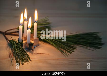 Vier kleine Adventskerzen, die auf einem Keksschneider in Sternform und einem Kiefernzweig auf einem Holztisch platziert sind, minimalistische Dekoration in der Weihnachtszeit, Stockfoto