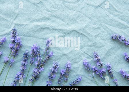 Lavendel blüht und hinterlässt einen kreativen Rahmen auf einem textilen Hintergrund. Draufsicht, flach liegend. Florale Komposition Stockfoto