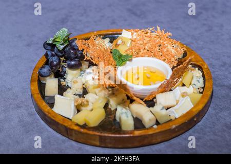 Käseplatte serviert mit Crackern, Trauben und Gläsern für Wein im Restaurant. Alter gouda-Käse auf Verkostungsteller. Bankettservice. Catering-Speisen. Buffet Stockfoto