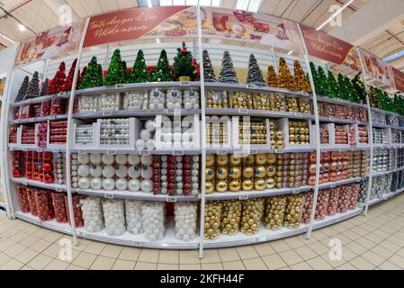 Cuneo, Italien - 18. November 2022: Weihnachtskugeln in verschiedenen Formen und Farben auf Regalen mit kleinen verzierten weihnachtsbäumen zum Verkauf in italienischen s Stockfoto