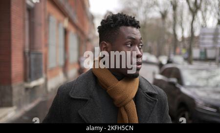 Eleganter junger schwarzer Mann, der während der Wintersaison auf dem Bürgersteig läuft und die Stadt erkundet oder pendelt Stockfoto