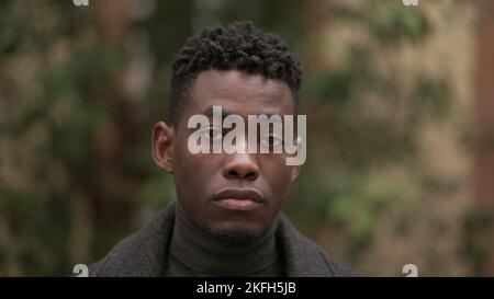 Hübscher junger schwarzer Mann, der im Freien steht und denkt Stockfoto