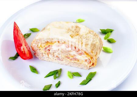 Eierrolle mit Fleisch, Käse und eingepickten Gurken in einer Platte, die mit Tomaten auf dem Tisch serviert wird. Horizontal Stockfoto