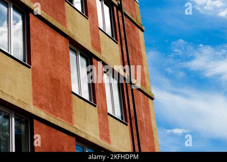 Ein minimalistisches Panelhaus mit einer frischen Fassade in Rot- und Gelbtönen. Die Fenster spiegeln den blauen, ruhigen Himmel wider. Das Konzept des Lebens in der Stadt Stockfoto