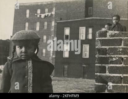 Junges Mädchen, mit anderen Kindern im Hintergrund, in einem freien Grundstück hinter einigen Mietshäusern, East Harlem, New York City, 1947 - 1951. Stockfoto