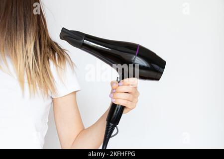 Das Mädchen trocknet ihre Haare mit einem Haartrockner auf weißem Hintergrund, Haartrockner und Haar, Friseur Stockfoto