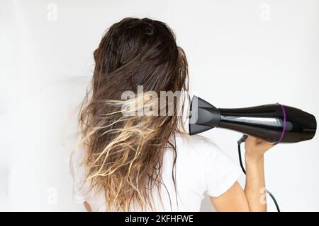 Das Mädchen trocknet ihre Haare mit einem Haartrockner auf weißem Hintergrund, Haartrockner und Haar, Friseur Stockfoto