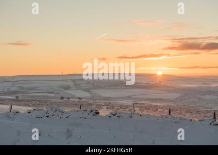 Die Sonne geht über dem Rossendale-Moorland auf. Düstere Moore, bedeckt mit Schnee, Windturbinen und Dampfpfaden in der Ferne. Wunderschöner Himmel. Stockfoto