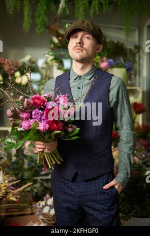 Attraktive fröhlich kaukasischen Männchen in Spitzenmütze und Vintage-Kleidung aus dem Jahr 20s mit schönen Bouquet von roten und violetten Blumen. Konzept zum Muttertag oder Valentinstag. Hochwertige Bilder Stockfoto