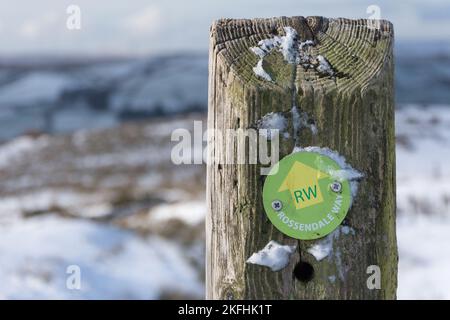 Rossendale Way Fußwegmarkierung auf einem Zaunpfahl im Schnee im Moorland bei Rossendale Valley. Mit Blick über das schneebedeckte Moorland. Stockfoto