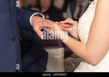 Die Braut legt den Ehering während der Hochzeitszeremonie auf den Finger des Bräutigams. Stockfoto