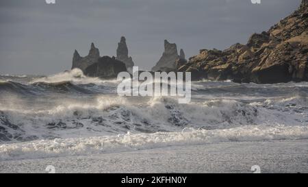 Ostseestapel in Vik, Island. Stürzende Meereswellen brechen am schwarzen Sandstrand mit Meeresnebel über den Wellen Stockfoto