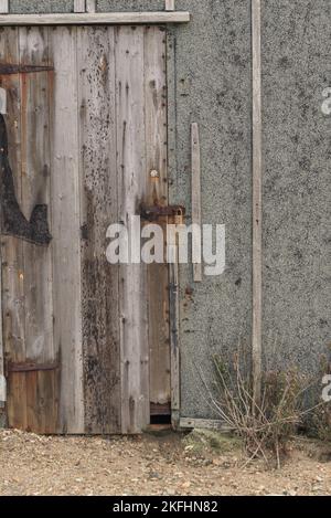 Nahaufnahme einer verrotteten, alten Schuhtür mit rostigem Vorhängeschloss. Betonwände und Sandsteine im Vordergrund. Stockfoto