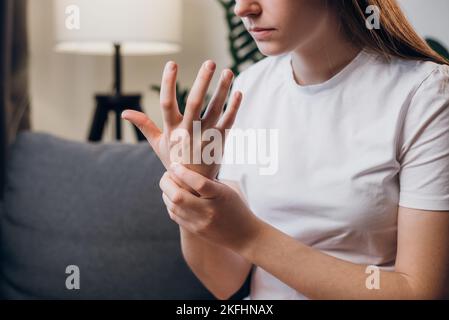 Nahaufnahme der weiblichen Arme mit schmerzhaftem Handgelenk, verursacht durch längere Arbeit am Computer oder Laptop, der auf der Couch sitzt. Karpaltunnelsyndrom, Arthritis, n Stockfoto