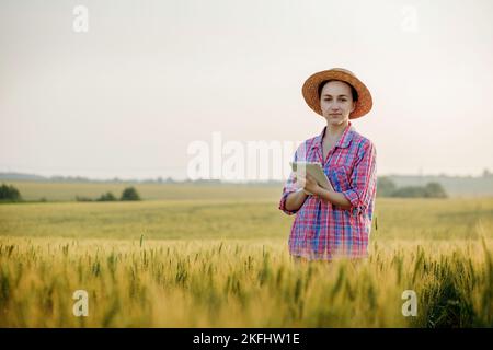 Ein junger Fcrmer überprüft ein Getreidefeld und sendet Daten von einer Tablette an die Wolke. Konzept von Smart Farming und digitaler Landwirtschaft. Erfolgreiche Produktion Stockfoto